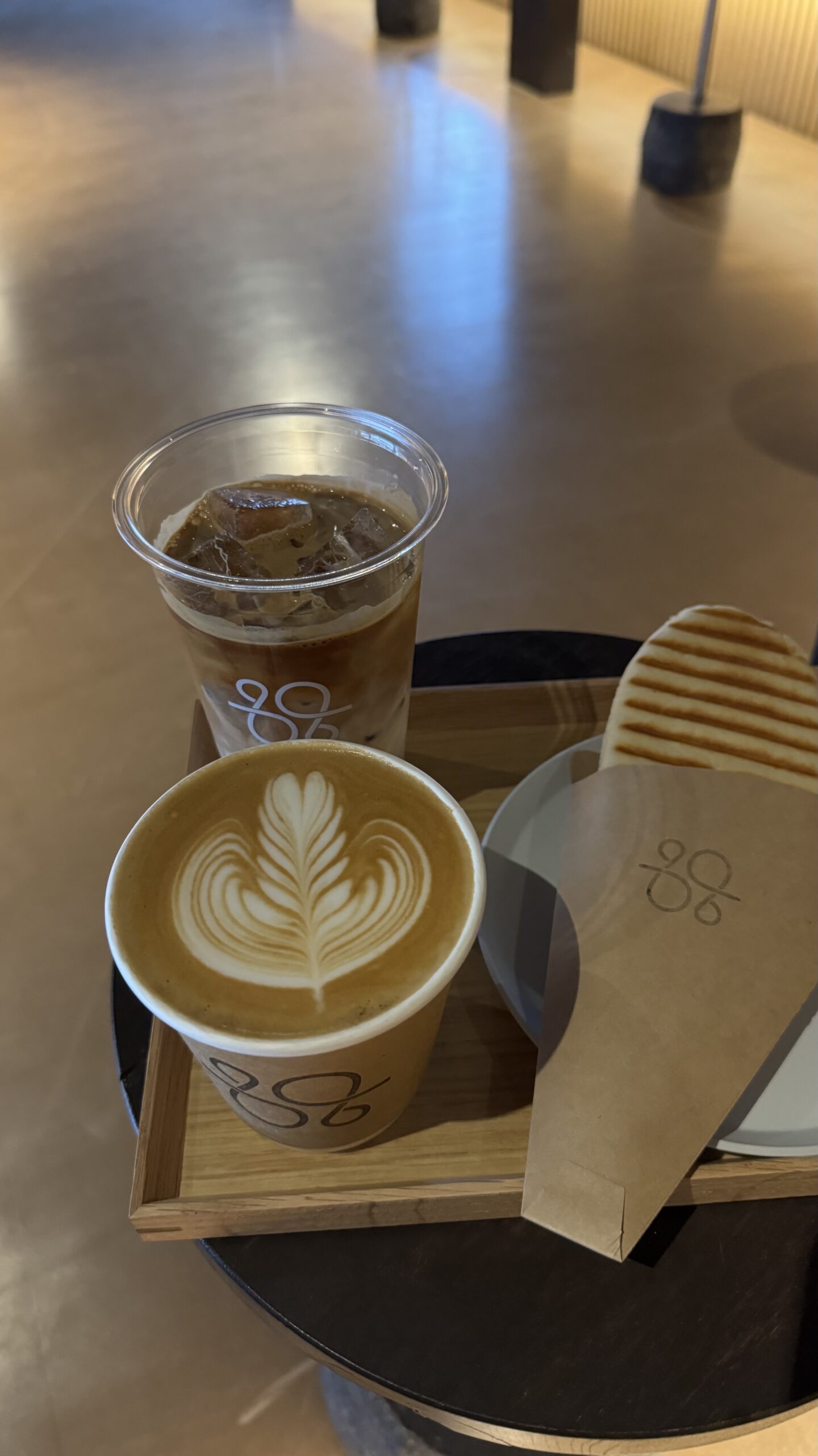 A tray from Sway Coffee Roaster holding a hot latte, an iced coffee, and a grilled panini.