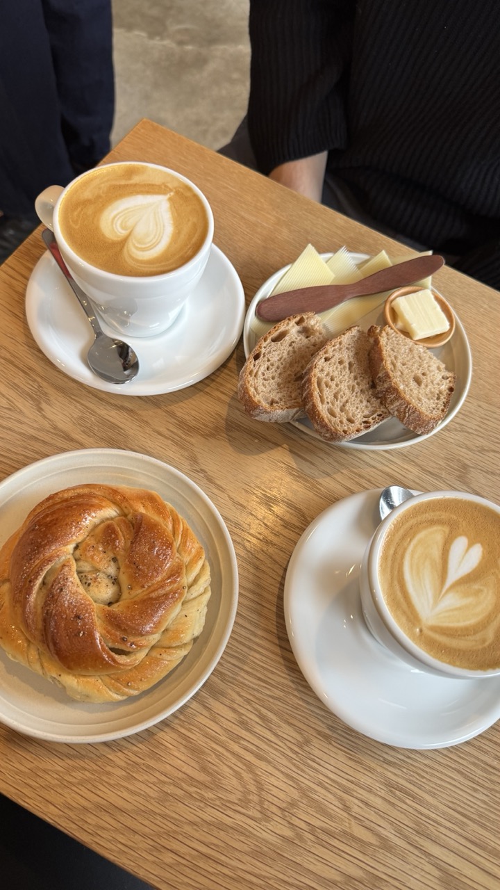 A breakfast spread at townsfolk coffee, featuring two lattes with heart-shaped art, a cardamom bun, and sliced bread.