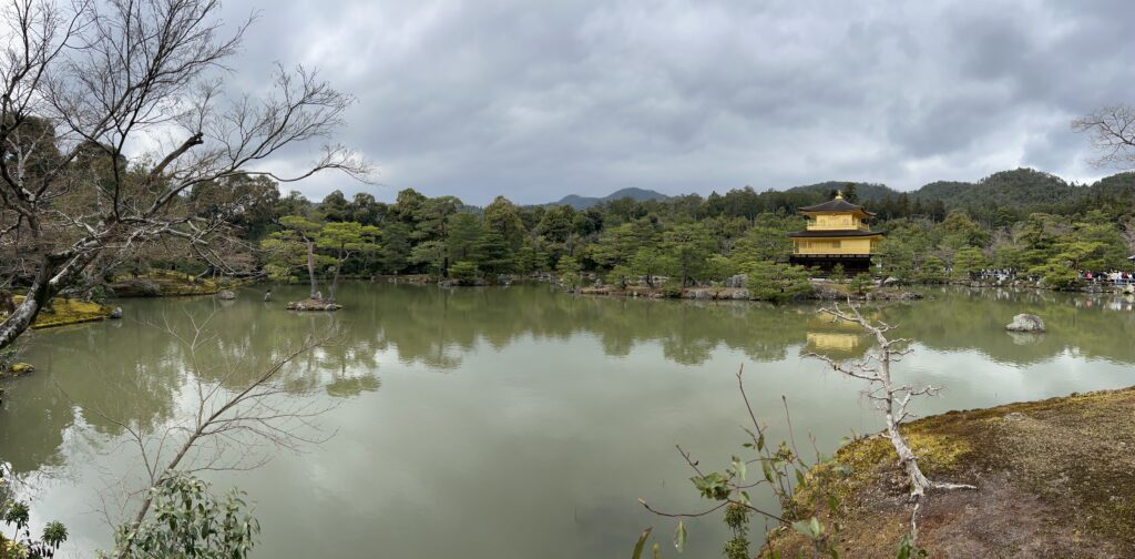 Kinkaku-ji, the Golden Pavilion, reflected across its pond in Kyoto beneath a cloudy sky.