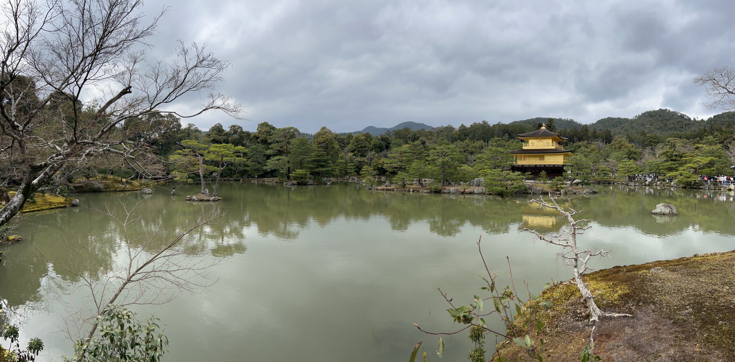 Kinkaku-ji, the Golden Pavilion, reflected across its pond in Kyoto beneath a cloudy sky.