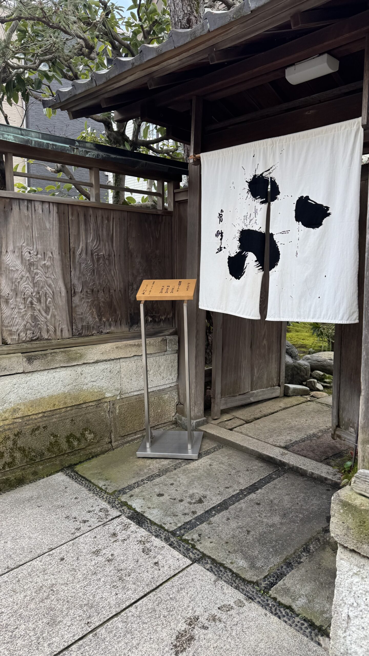 A noren curtain hanging in a wooden doorway on a stone path in Kanazawa.