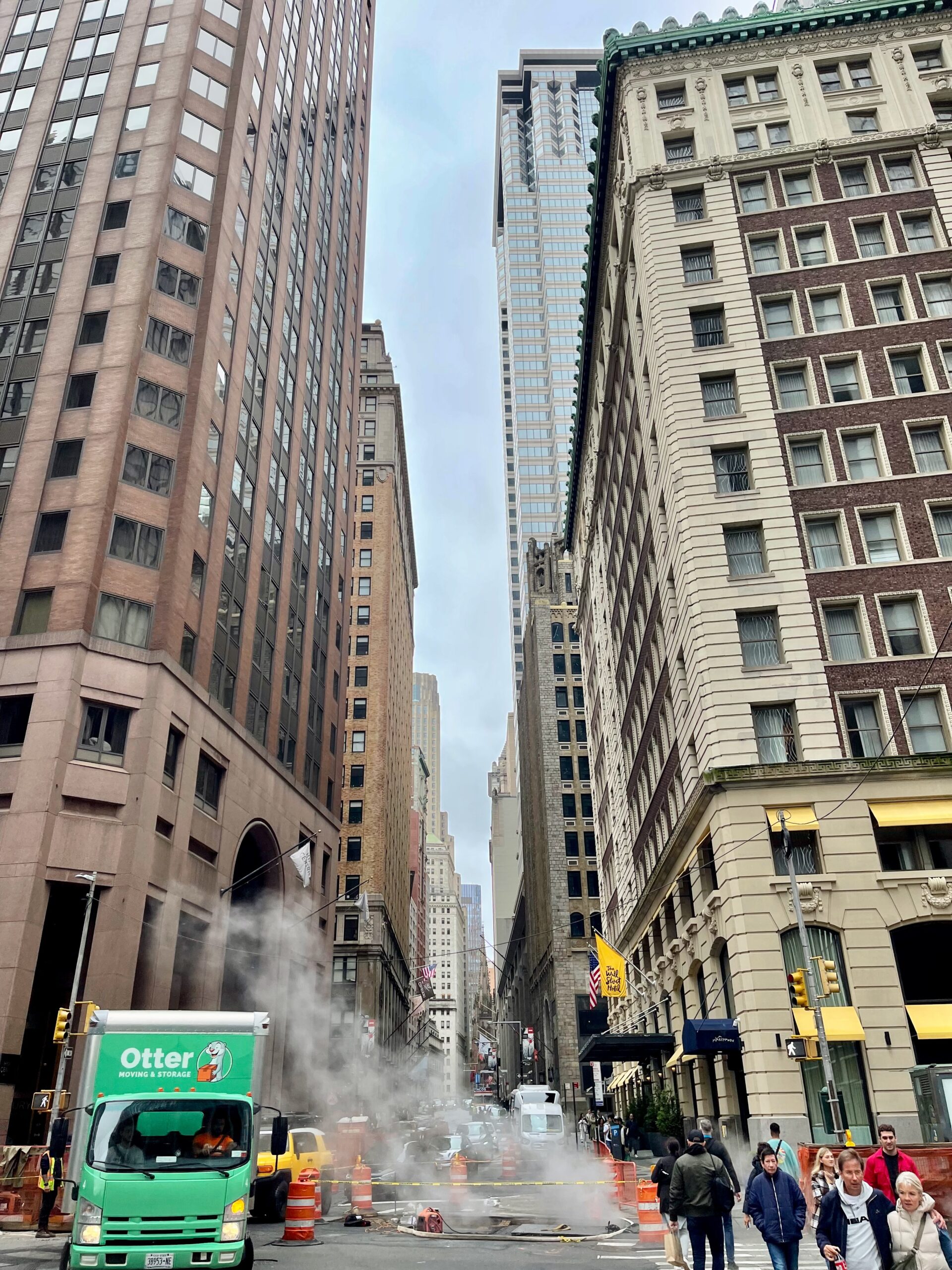 Financial District street near Wall Street, with tall buildings and steam rising from roadworks.